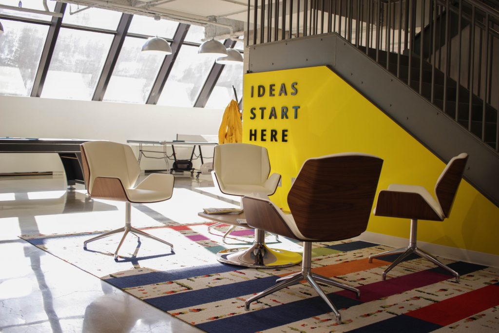 empty chairs in a circle in front of a bright yellow wall that reads "Ideas Start Here"