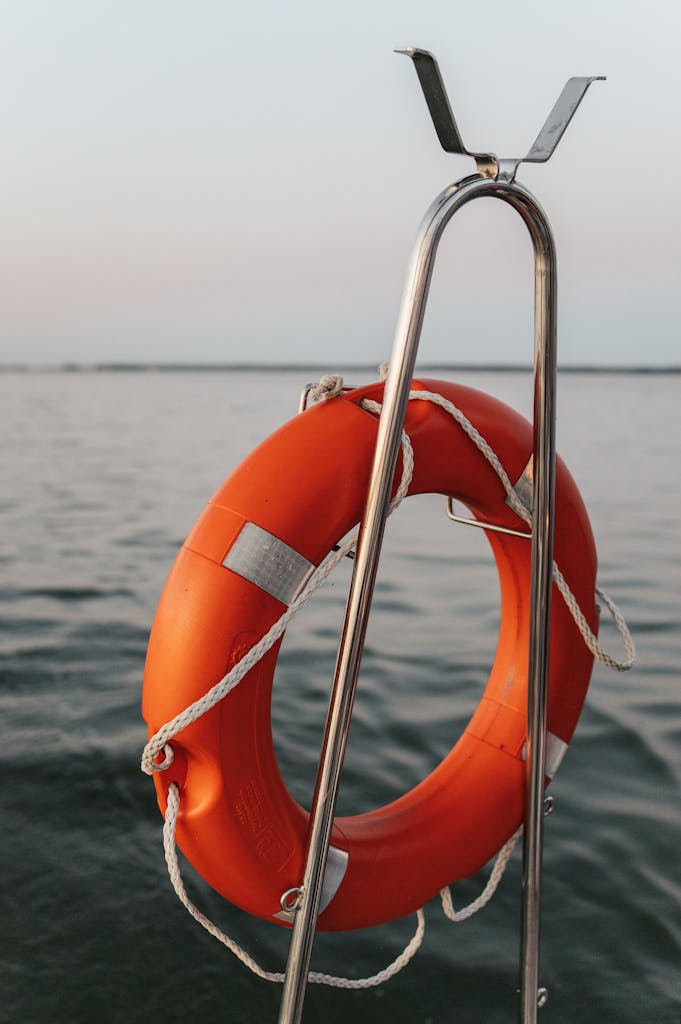 A bright orange lifebuoy hangs on a boat over still serene waters, symbolizing safety and preparation.